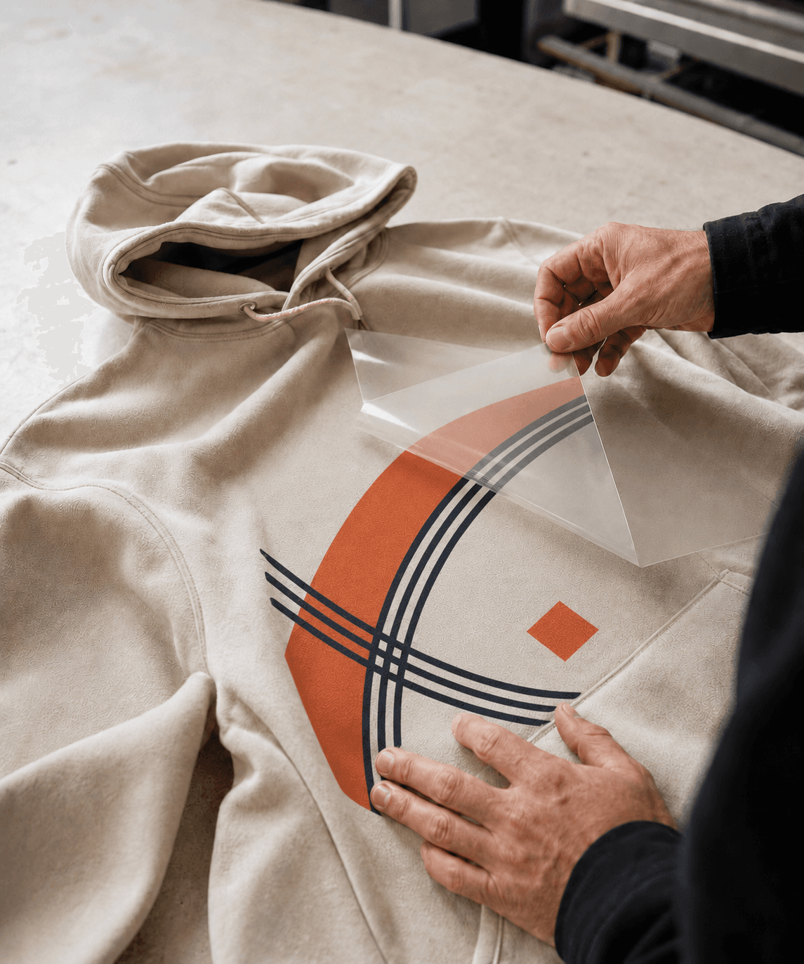 A clear DTF transfer being peeled from a custom printed stone hoodie.